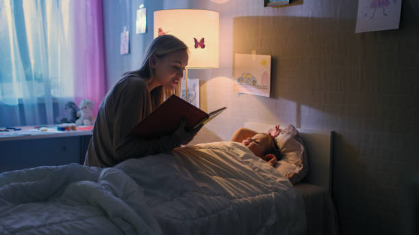 la giovane madre amorevole legge le storie della buonanotte alla sua piccola bella figlia che va a dormire nel suo letto. - child reading mother book foto e immagini stock