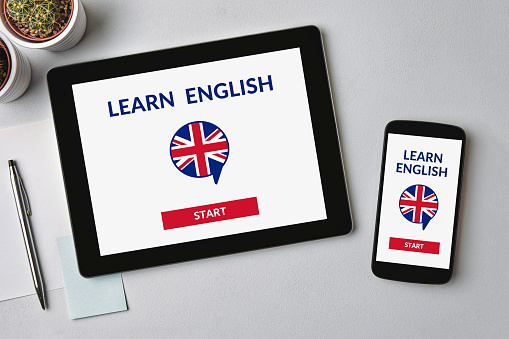 Learn English concept on tablet and smartphone screen over gray table. Flat lay