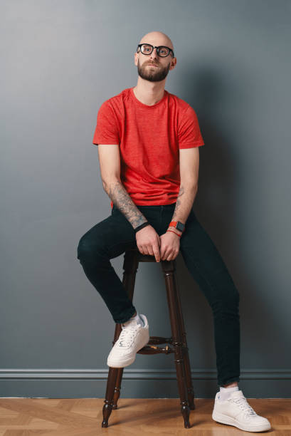 istock Confident young man posing in the studio on gray background while sitting on a tall chair 1158169387