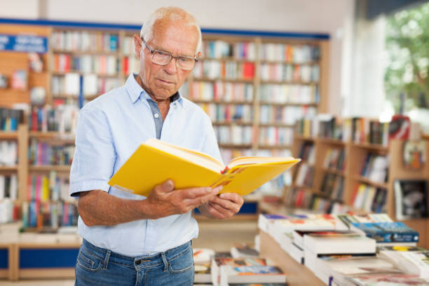 istock Focused older man looking inside of books while visiting bookstore 1158172422