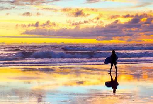 Surfer walking by the beach with surfboard at sunset. Bali, Indonesia