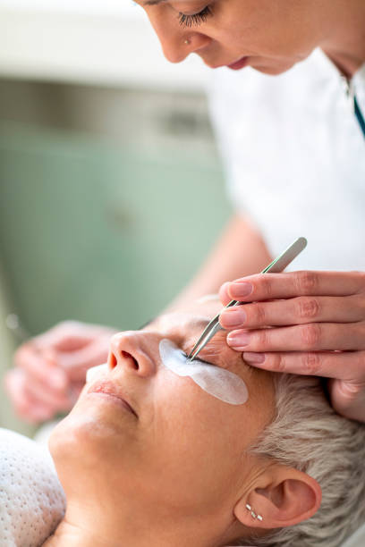 istock Elderly woman lying down on a cosmetic parlor bed getting her eyebrows done by a professional beautician 1158177067