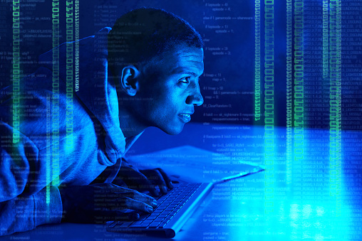 Shot of a young male hacker cracking a computer code in the dark