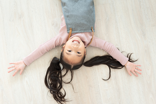 Smiling Asian child girl wear pink sweater and apron lying on wooden floor.