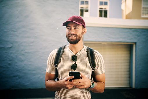 Cropped shot of a handsome young man standing alone and holding his cellphone in the city during the day