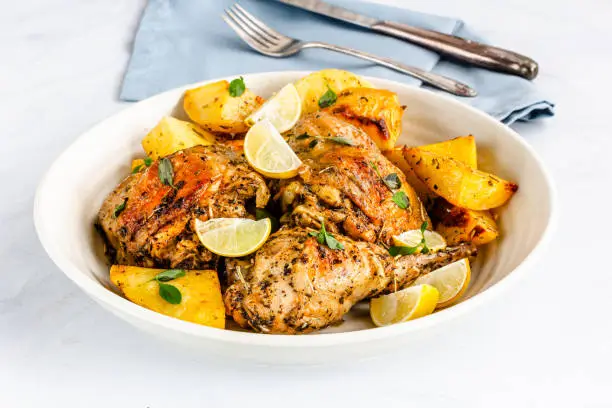 Greek Lemon Chicken with Potatoes in a Bowl on White Background. Baked Chicken and Potatoes on a Sheet Pan Garnished with Fresh Oregano Leaves."n