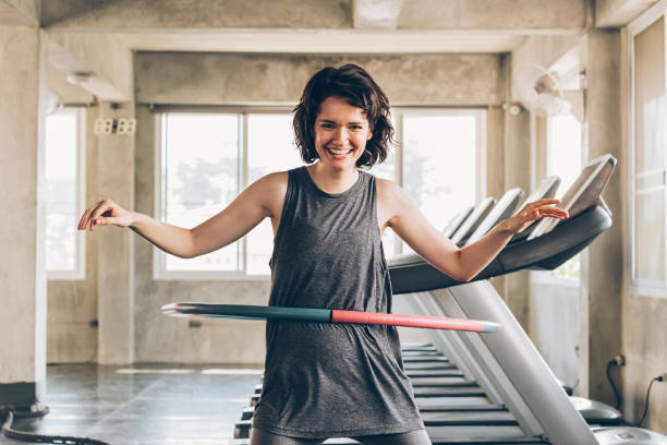 joven sonriendo feliz mujer deportiva caucásica jugando hula hoop dentro del estudio de gimnasio - hooping fotografías e imágenes de stock