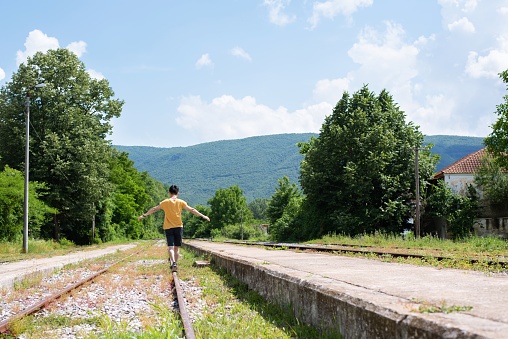 A mid adult man playfully balancing on a train track in rural Greece on a sunny day.