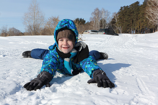 Happy cheerful boy lying in the snow in winter
