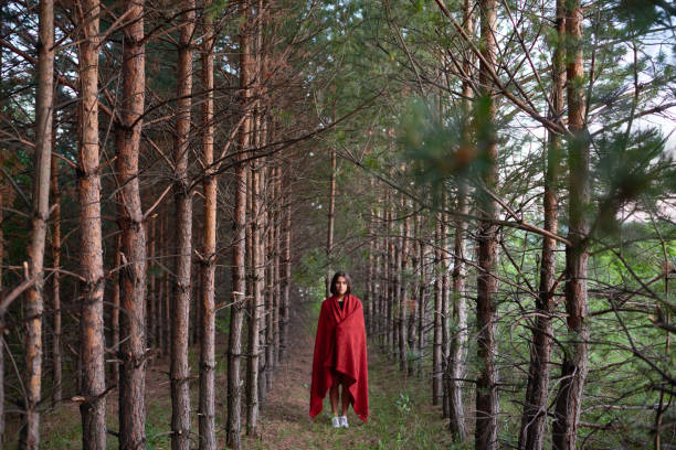 istock Girl in red fabric standing alone in woods 1158183513
