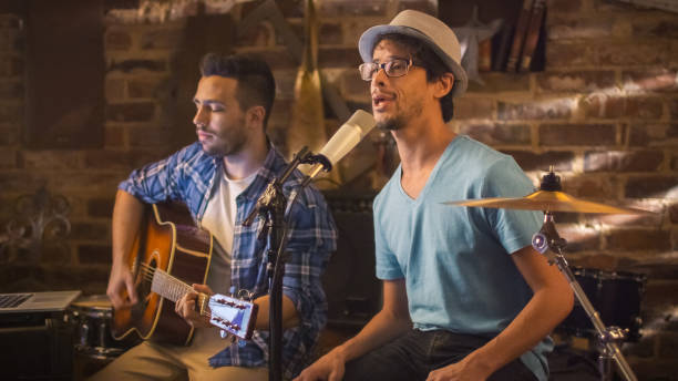 istock Two young man sing and play guitar while recording a song in a home studio in a garage. 1158183664