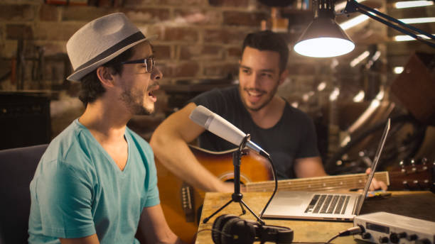 istock Two young man sing and play guitar while recording a song in a home studio in a garage. 1158183698