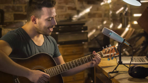 istock Young man is singing and playing guitar while making an audio recording at home in a garage. 1158183753