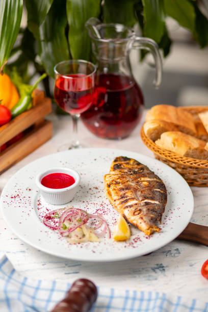 Roasted grilled fish served with herbs, lemon,  onion salad and dip red tomato sauce.