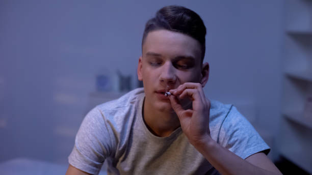 adolescente maschio che fuma in edicolazione, serata a casa, esperimento di età imbarazzante - narcotic teenager marijuana drug abuse foto e immagini stock