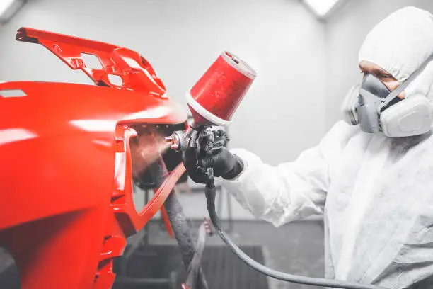 Photo of Professional male car painter is painting in garage by airbrush. Man works with spray gun.