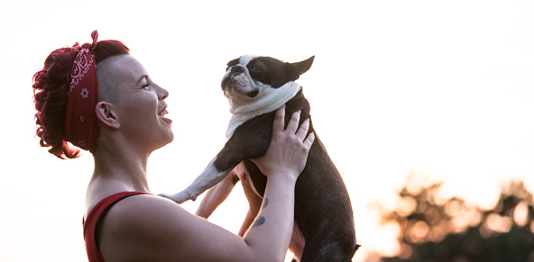 Smiling Young Woman Holding Her Boston Terrier in the Air.
