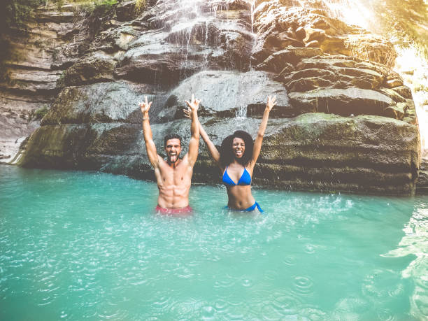 pareja de influenciades de viaje divirtiéndose bajo cascadas del río - jóvenes nadando dentro de la laguna de agua esmeralda - verano, nuevo concepto de trabajos de moda y concepto de amistad - enfoque en las caras de los chicos - waterfall thailand tropical rainforest tropical climate fotografías e imágenes de stock