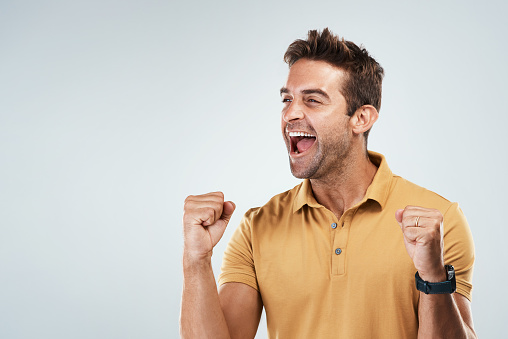 Studio shot of a cheerful young man punching the air in excitement while standing against a grey background