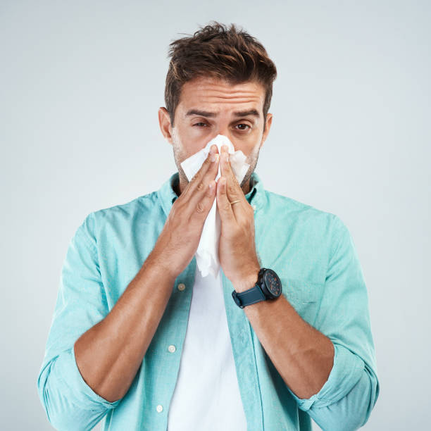 Yeah I'm getting sick again Portrait of a young man blowing his nose with a tissue while standing against a grey background cold and flu man stock pictures, royalty-free photos & images