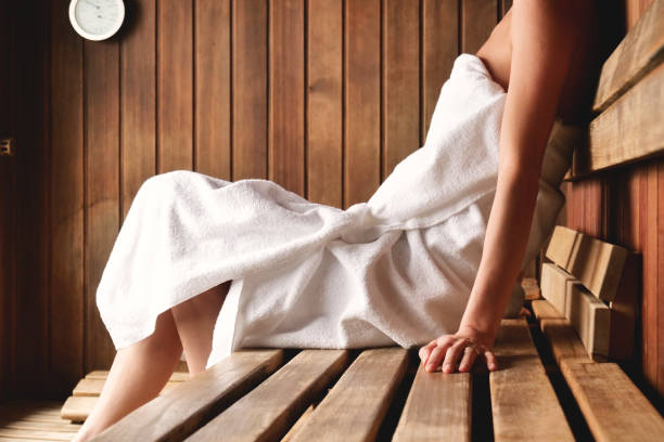 une belle femme portant une serviette blanche prend un sauna: le sauna est en bois avec une grande fenêtre avec vue sur la neige. - sauna photos et images de collection