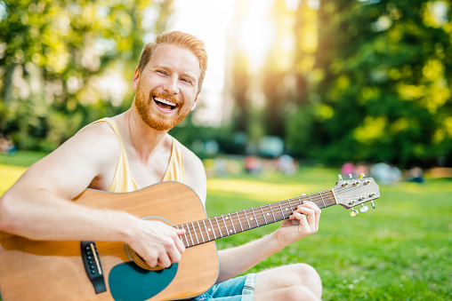 Happy young hipster man playing a guitar in the park.
