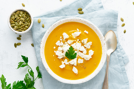 Pumpkin cream soup with feta cheese, autumn homemade food, white background, top view, seasonal vegeterian dish