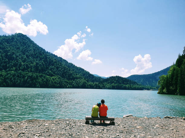 Young couple sitting on bench at Ritsa lake background in Abkhazia at summer sunny day