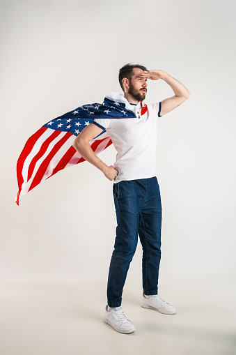 Celebrating an Independence day. Stars and Stripes. Young man with the flag of the United States of America isolated on white studio background. Looks crazy happy and proud as a patriot of his country.