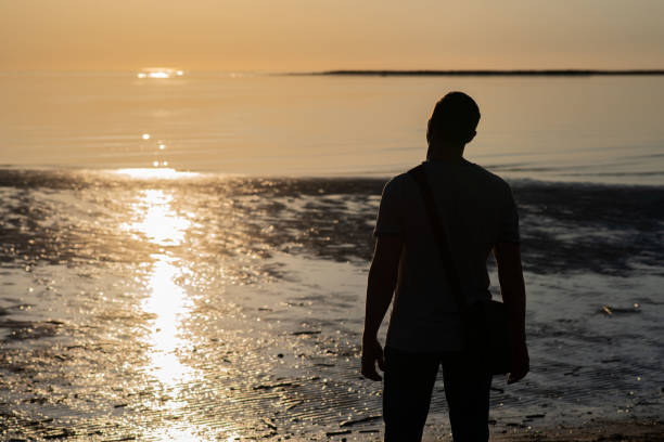 istock man stands on the seashore at sunset 1158219142