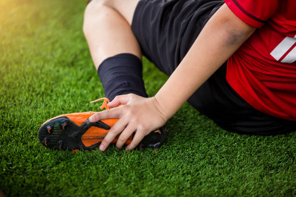 footballer is sitting and catch the ankle of the feet because of pain, soccer player was injured in the foot footballer is sitting and catch the ankle of the feet because of pain, soccer player was injured in the foot with pain during competition or practice. physical injury sport ice pain stock pictures, royalty-free photos & images