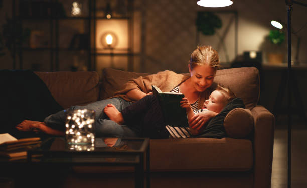 la famiglia prima di andare a letto la madre legge al libro del figlio vicino a una lampada la sera - bedtime stories foto e immagini stock