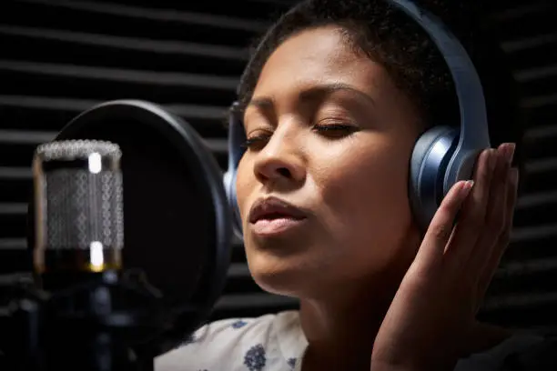 Photo of Female Vocalist Wearing Headphones Singing Into Microphone In Recording Studio
