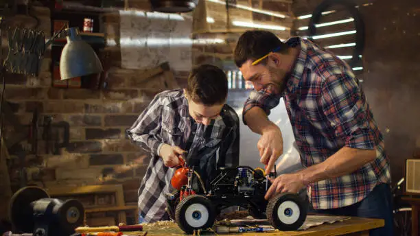 Photo of Father and son are working on a radio control toy car in a garage at home.