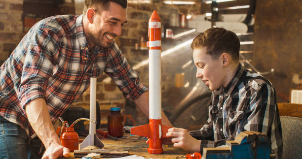 Father and son are modeling a toy rocket in a garage at home. Father and son are modeling a toy rocket in a garage at home. model rocket stock pictures, royalty-free photos & images