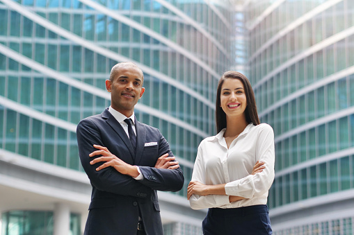 Portrait of a business man and woman of different ethnicity are smiling in the camera with their arms crossed. Concept of success, finance and team and cooperation.