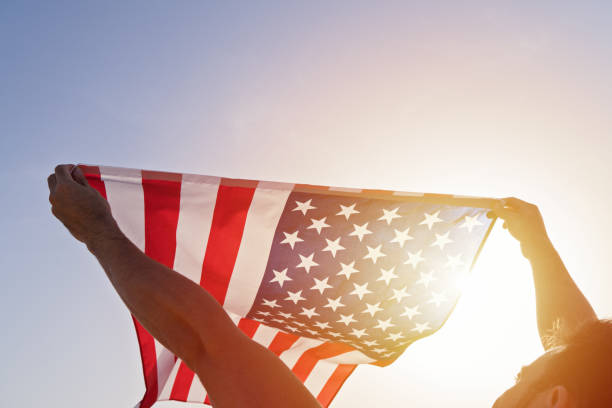 mann erhoben hände mit winkenden amerikanischen flagge gegen klaren blauen himmel - human hand waving human arm high angle view stock-fotos und bilder