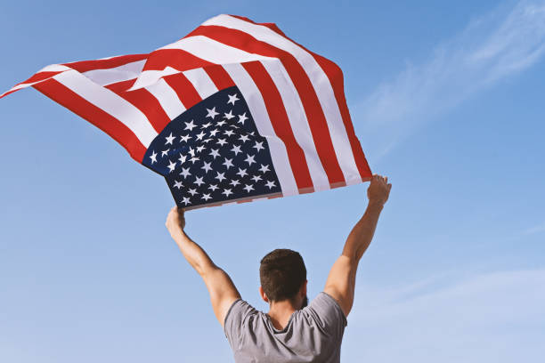 istock Man from behind with raised hands and waving American Flag 1158233171