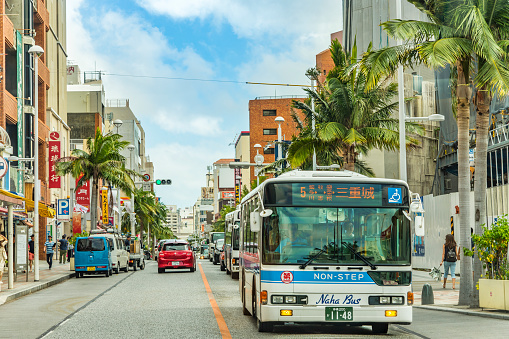 Naha, Japan - September 16 2018: Naha city non-step bus running through palm tree lined streets under Okinawa blue summer sky