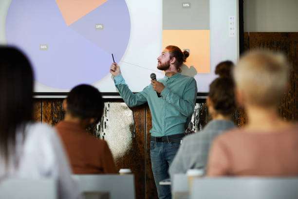 Business Seminar Portrait of contemporary bearded man giving presentation standing by projector screen in lecture hall, copy space teacher projector stock pictures, royalty-free photos & images