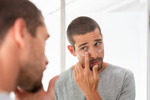 homme appliquant la crème hydratante sous des yeux - human skin aging process beautiful hygiene photos et images de collection