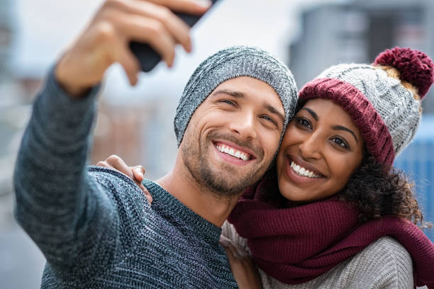Smiling multiethnic couple taking selfie in winter Happy multiethnic couple in the city taking selfie in a winter day. Smiling man and african girl taking selfie with smartphone during winter on street. Young woman and cheerful guy on christmas holidays taking photo. black man white woman couple stock pictures, royalty-free photos & images