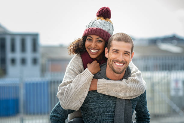 coppia che si gode il giro in piggyback in inverno - fun knit hat adult dating foto e immagini stock