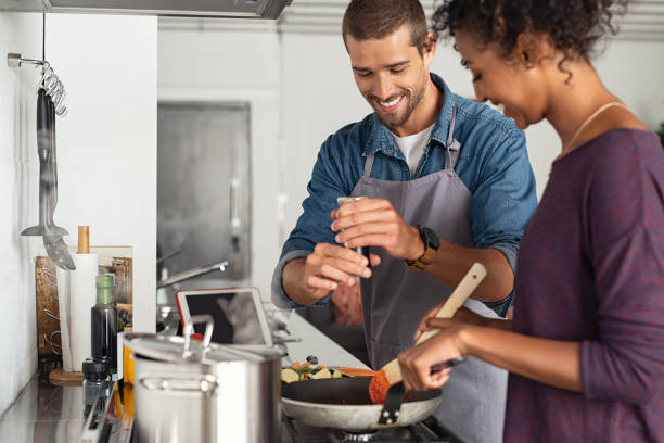 Man adding pepper in tomato sauce Young man cooking with girlfriend and adding spice to the sauce. Guy adds black pepper into frying pan on stove while woman using spatula to mix. Multiethnic couple preparing lunch together at home. sauce photos stock pictures, royalty-free photos & images