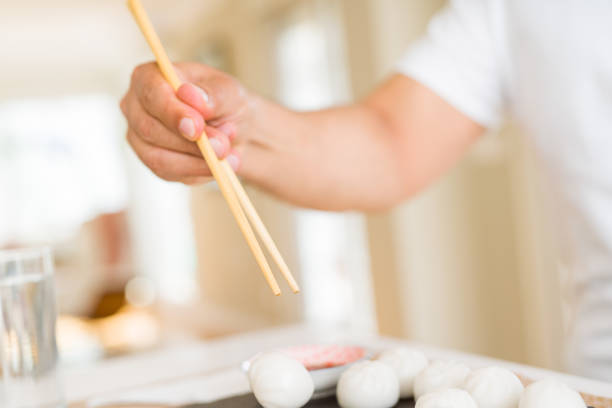 Middle age man eating asian dim sum using chopsticks at home