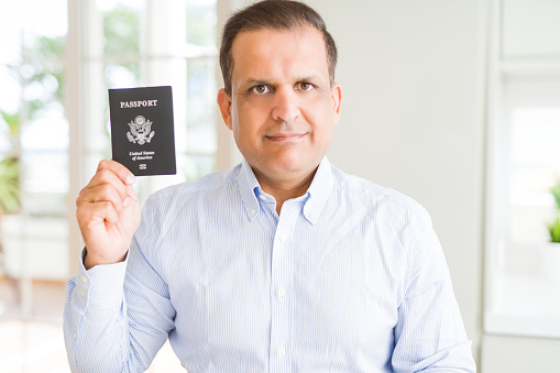 Middle age man holding holding passport of United States with a confident expression on smart face thinking serious