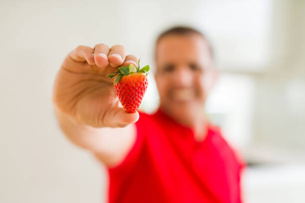 Middle age man holding strawberry and smiling