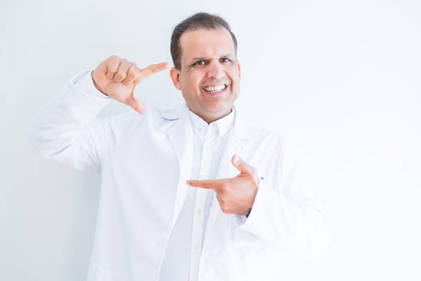 Middle age doctor man wearing medical coat over white background smiling making frame with hands and fingers with happy face. Creativity and photography concept.