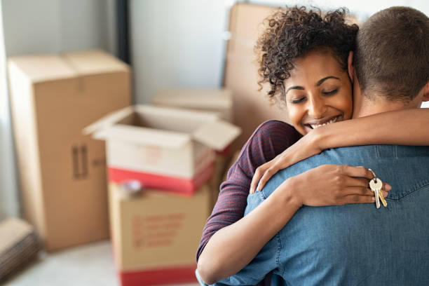 Woman hugging man and holding home keys Young african woman holding home keys while hugging boyfriend in their new apartment after buying real estate. Lovely girl holding keys from new home and embracing man. Happy couple in their apartment around cardboard boxes. new home stock pictures, royalty-free photos & images
