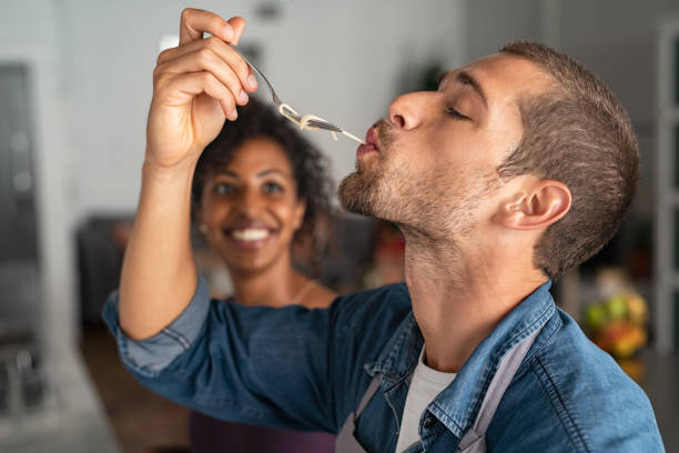 Man tasting spaghetti Man tasting spaghetti pasta while smiling woman look at him. Closeup face of young man tasting meal while cooking at home. Handsome guy eating noodles with fork in kitchen and feel if the recipe is right. tasting stock pictures, royalty-free photos & images